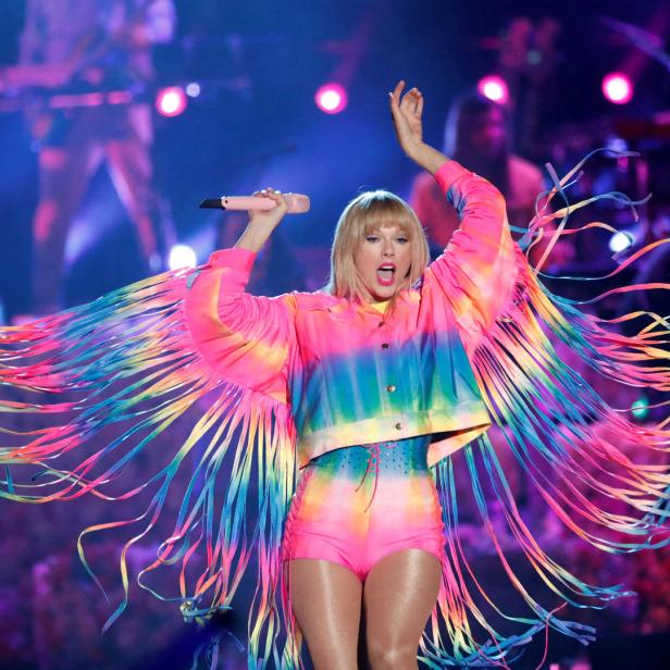 Taylor Swift tritt in einem farbenfrohen Outfit mit Fransenärmeln auf einer Bühne auf.