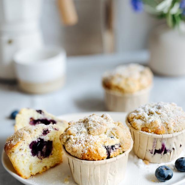 Ein Teller mit Blaubeermuffins, bestreut mit Puderzucker, neben einer Kaffeekanne.
