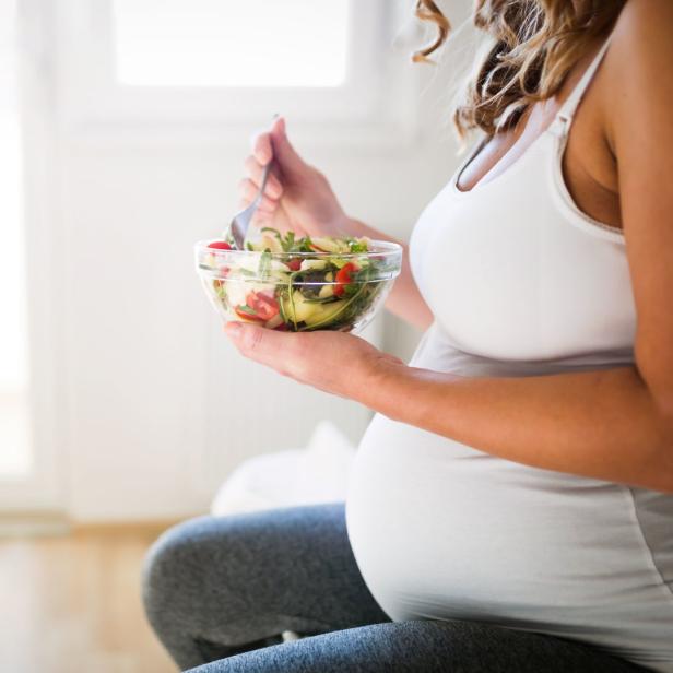 Eine schwangere Frau isst einen Salat mit Tomaten und Avocado.