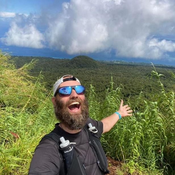 Torbjørn Pedersen steht auf einem Berg mit üppiger Vegetation im Hintergrund.