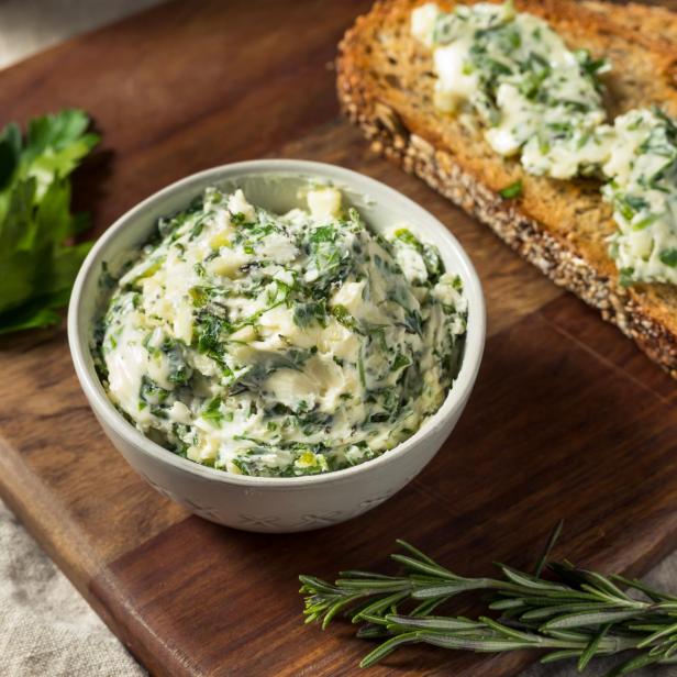 Kräuterbutter in einer Schüssel und auf Brot auf einem Holzbrett.