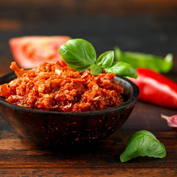 Ein Schälchen Pesto Rosso mit Basilikum, Tomaten und Chili auf einem Holztisch.