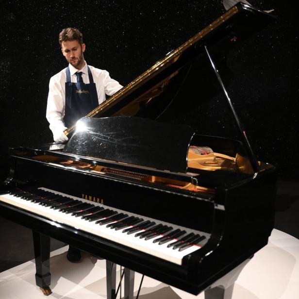 Ein Mann mit Schürze steht an einem schwarzen Yamaha-Flügel.