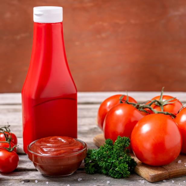 Eine Flasche Ketchup, eine Schale Ketchup und frische Tomaten auf einem Tisch.