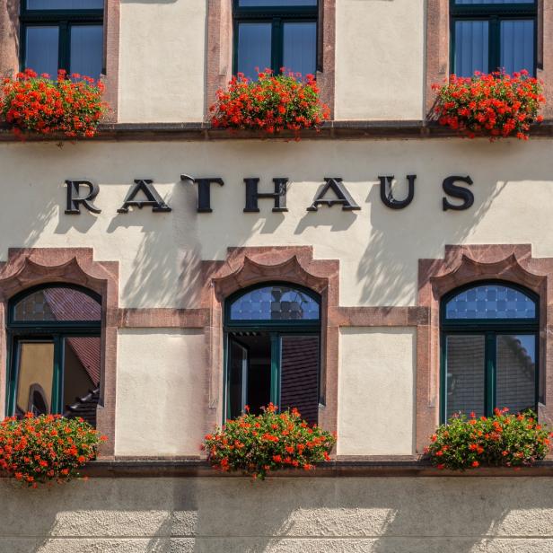Die Fassade eines Rathauses mit roten Blumen vor den Fenstern.