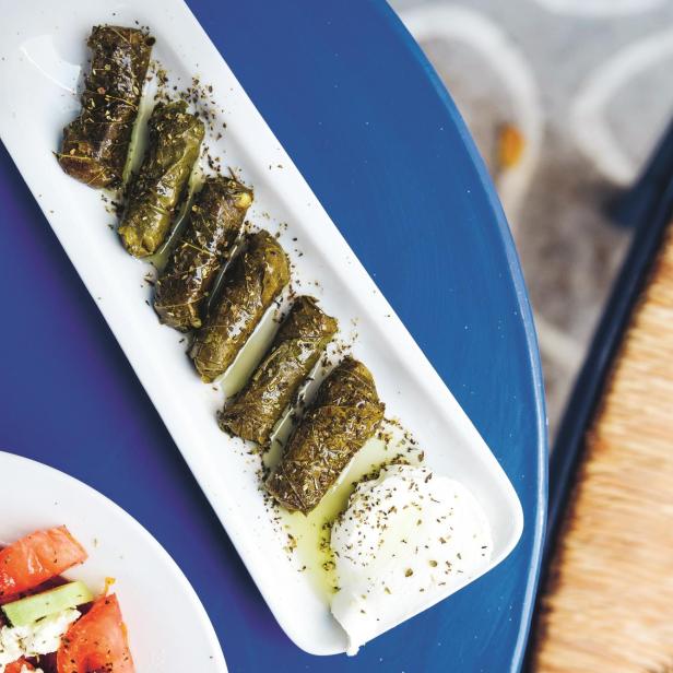 Dolmadakia mit Joghurt und griechischem Salat auf einem blauen Tisch.