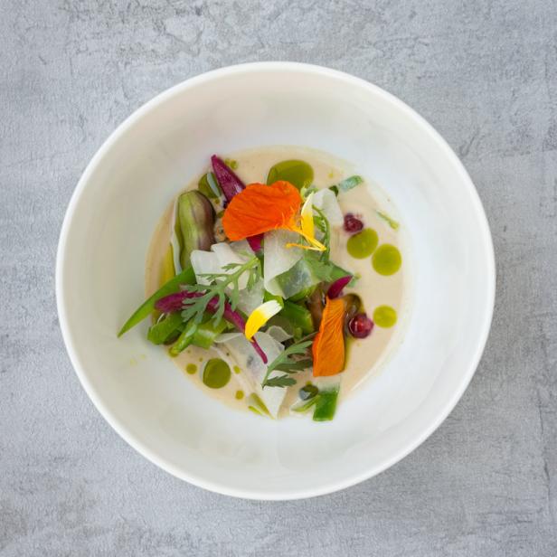Eine Schüssel mit kunstvoll angerichtetem Gemüse und Blüten in heller Sauce.