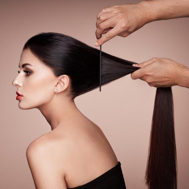 Ein Friseur kämmt das lange, dunkle Haar einer Frau.