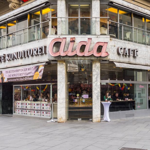 Das Café Konditorei Aida mit seiner markanten Leuchtreklame in einer Stadtszene.