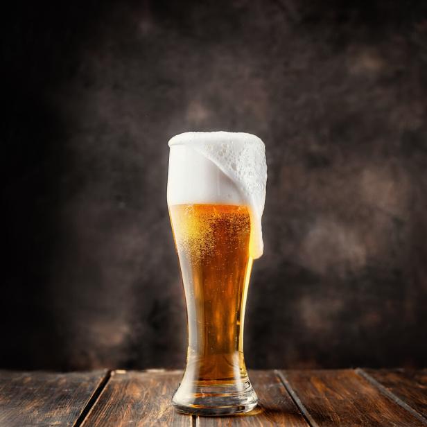 Ein Glas helles Bier mit viel Schaum auf einem Holztisch.