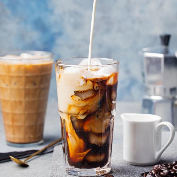 In ein Glas mit Eiswürfeln und Kaffee wird Milch gegossen.