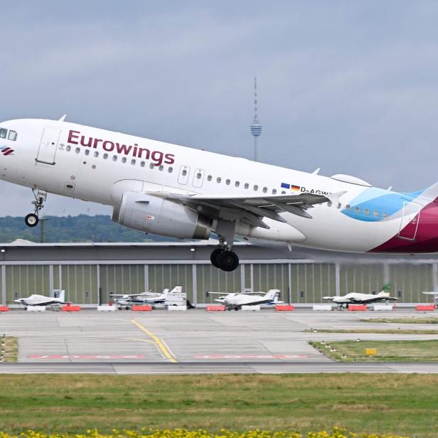 Ein Passagierflugzeug der Fluggesellschaft Eurowings hebt von einer Startbahn ab, im Hintergrund stehen kleinere Flugzeuge.