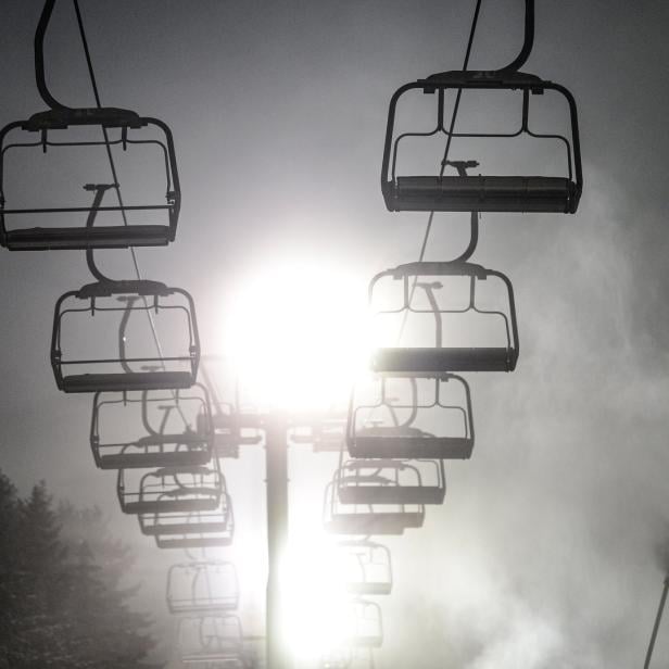 Eine Gondelbahn hängt im Nebel über einer Skipiste.