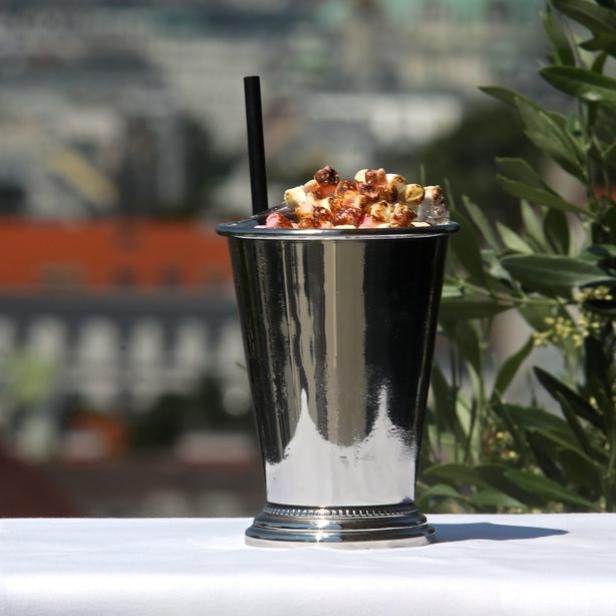 Ein silberner Becher mit Marshmallows und einem Strohhalm vor einer Stadtkulisse.