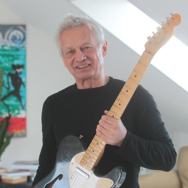 Ein lächelnder Mann mittleren Alters hält eine E-Gitarre der Marke Fender.