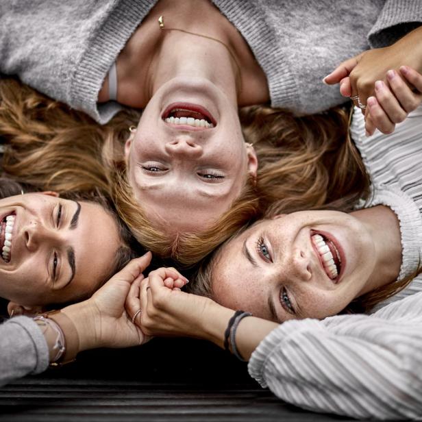 Drei glückliche junge Frauen liegen auf einer Bank und halten Händchen.