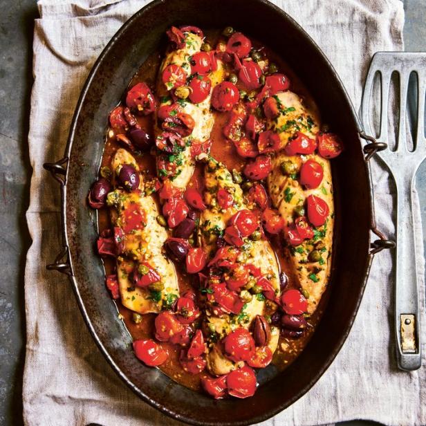 Hähnchenbrust mit Tomaten, Oliven und Kapern in einer dunklen Pfanne.