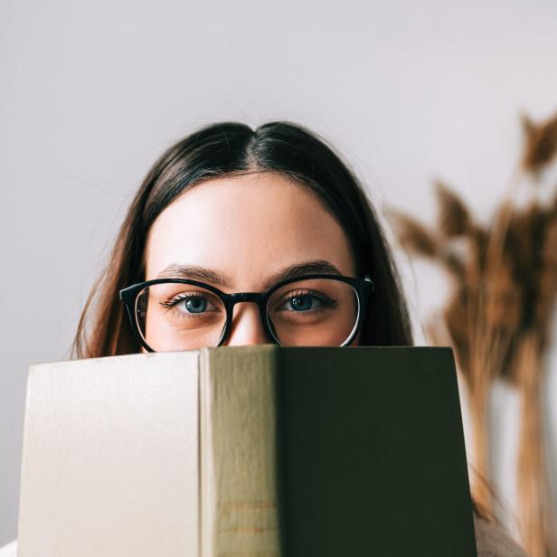 Eine Frau mit Brille versteckt ihr Gesicht hinter einem Buch.