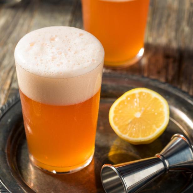 Ein Glas Aperol-Bier mit Zitronenscheiben auf einem silbernen Tablett.