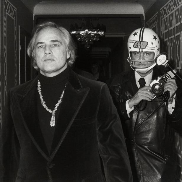 Marlon Brando und ein Fotograf mit Footballhelm stehen in einem Flur.