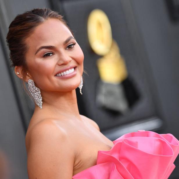 Chrissy Teigen lächelt in einem pinkfarbenen Kleid und auffälligen Ohrringen.