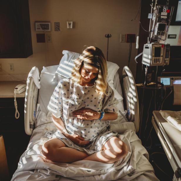 Eine schwangere Frau berührt ihren Bauch, während sie in einem Krankenhausbett sitzt.