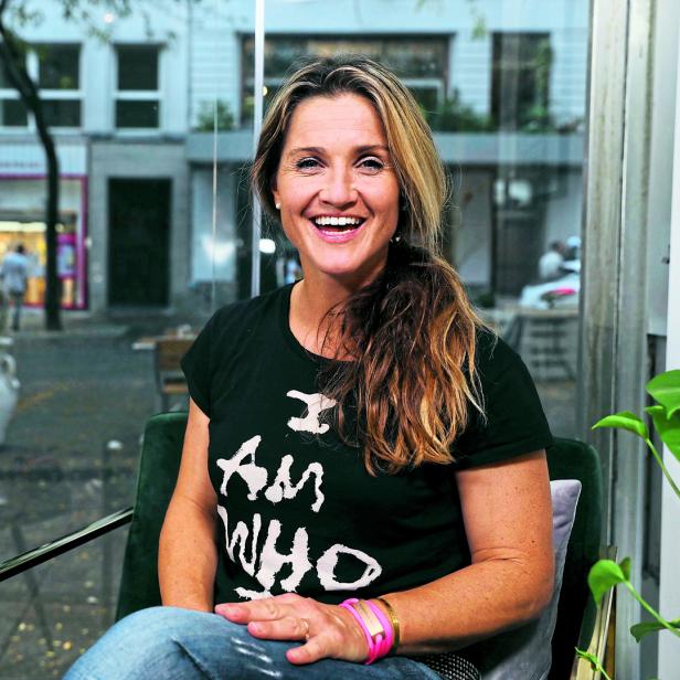 Eine lächelnde Frau sitzt in einem Café mit Blick auf die Straße.