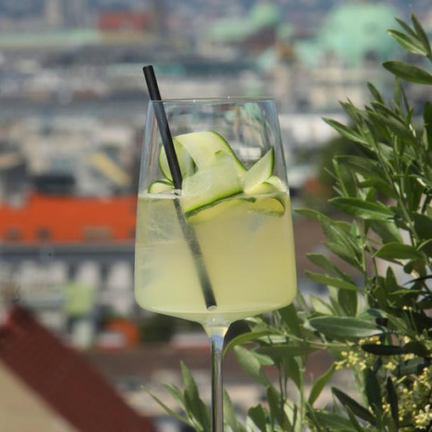 Ein Cocktail mit Gurke vor einer unscharfen Stadtkulisse.