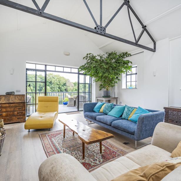 Ein helles Wohnzimmer mit blauen und beigen Sofas, einem gelben Sessel und einer großen Zimmerpflanze.