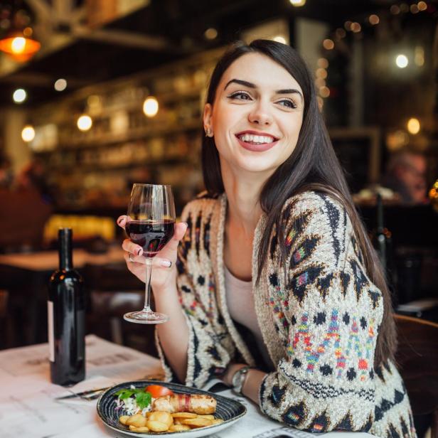 Eine Frau sitzt lächelnd in einem Restaurant mit einem Glas Rotwein.