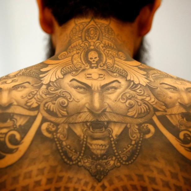 Ein Mann mit einem detaillierten Tattoo von drei Gesichtern auf seinem Rücken.