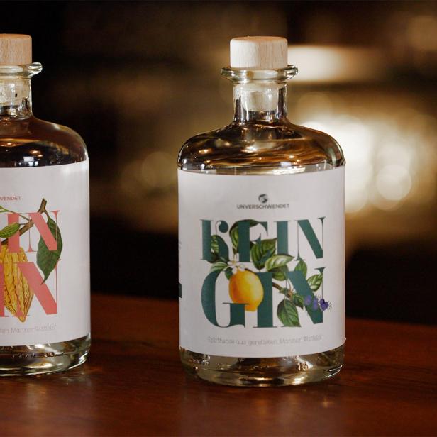 Zwei Flaschen „Unverschwendet Rein Gin“ und ein Glas mit Eiswürfeln auf einem Tisch.