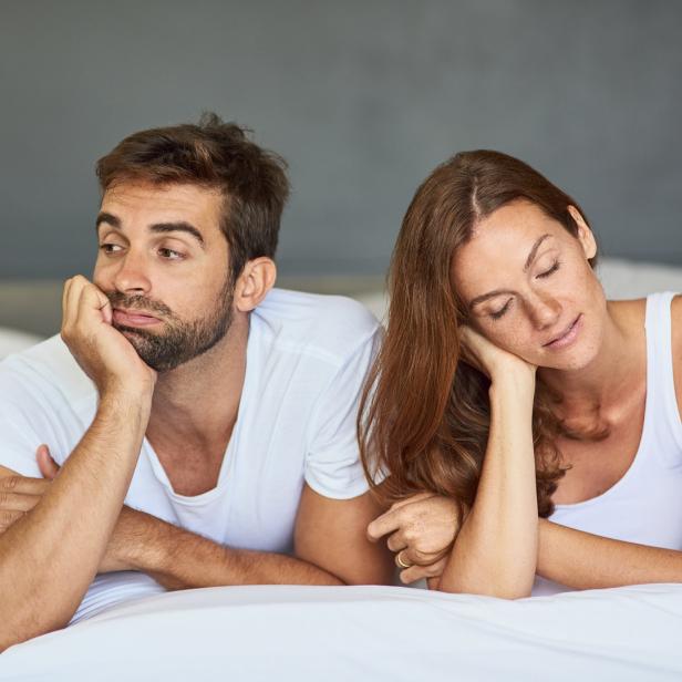 Ein Mann liegt gelangweilt im Bett, während eine Frau neben ihm schläft.