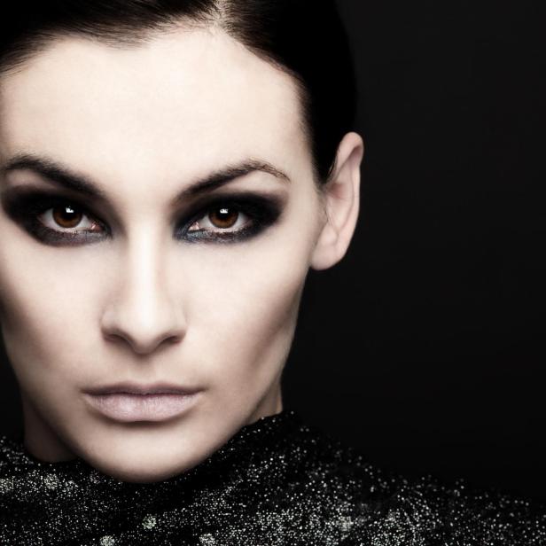 Eine Frau mit dunklem, dramatischem Make-up blickt in die Kamera.