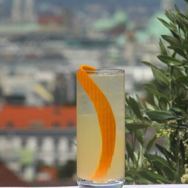 Ein Cocktail mit Orangenschale vor der Skyline von Wien.