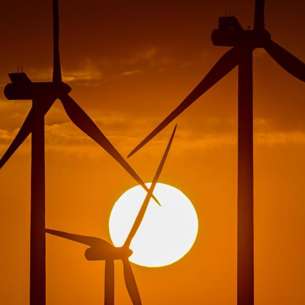 Windräder stehen im Gegenlicht der untergehenden Sonne.