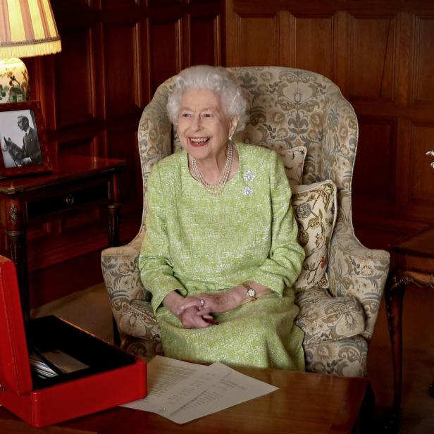 Königin Elizabeth II. sitzt lächelnd in einem Sessel in einem Wohnzimmer.