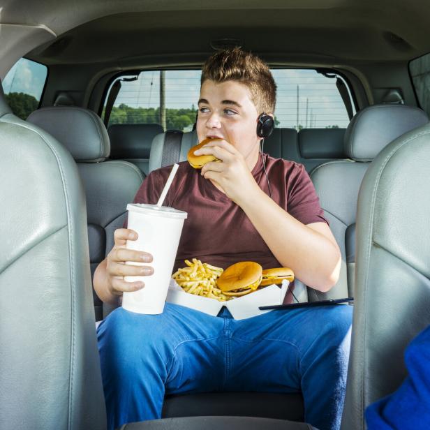 Ein Teenager im Auto isst Burger und Pommes.