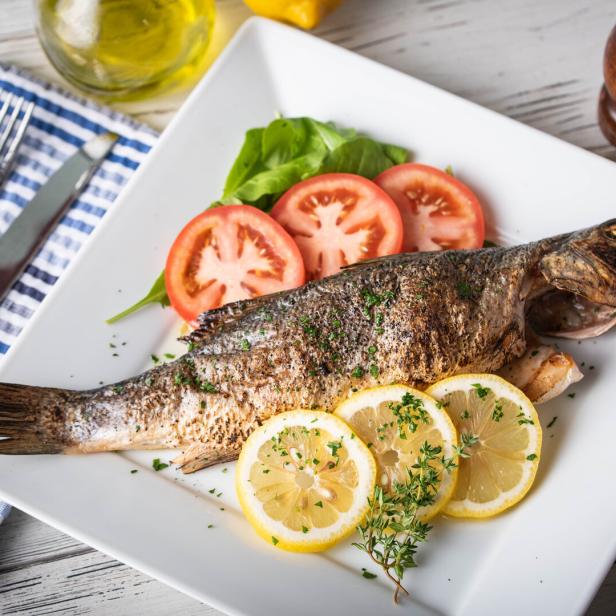Ein gegrillter Fisch wird mit Zitronen- und Tomatenscheiben auf einem Teller serviert.
