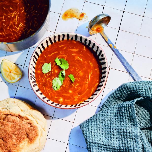 Eine Schüssel Harira-Suppe mit Koriander garniert, zusammen mit Brot und Zitrone.