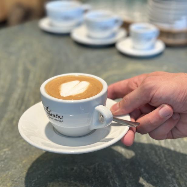 Eine Hand serviert eine Tasse Cappuccino mit Herzmuster auf dem Milchschaum.