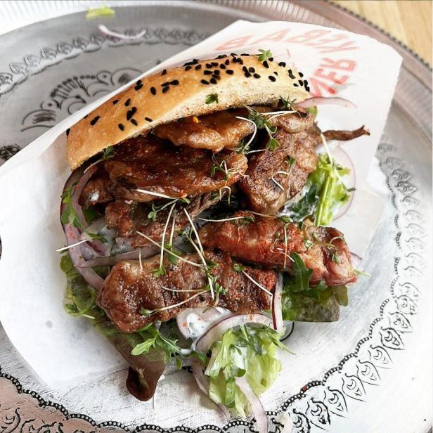Ein Döner-Sandwich mit Fleisch, Salat und roten Zwiebeln auf einem verzierten Teller.