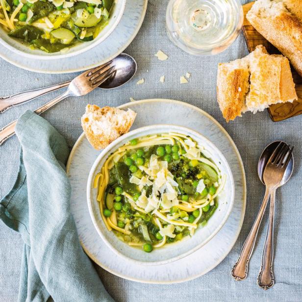 Zwei Schalen Minestrone Verde mit Nudeln, Erbsen und Parmesan auf einem Tisch.