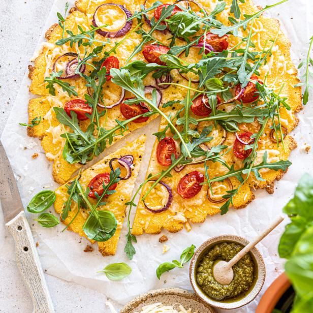 Eine Polenta-Pizza mit Tomaten, roten Zwiebeln und Rucola wird serviert.