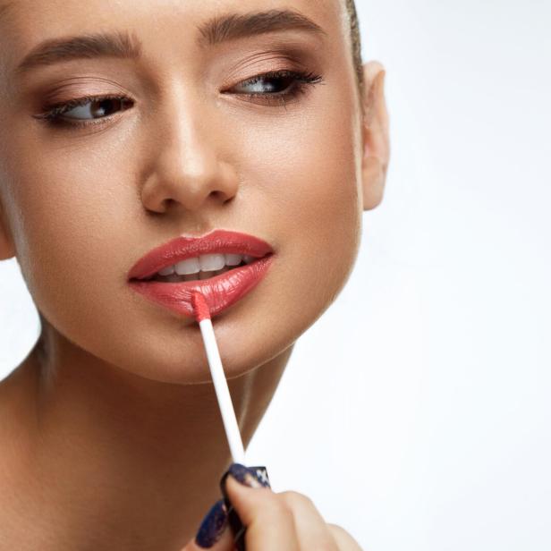 Eine Frau trägt Lipgloss auf ihre Lippen auf.