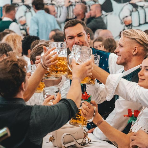 Menschen in Tracht stoßen mit Bierkrügen auf dem Oktoberfest an.
