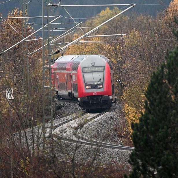 Ein roter Doppelstockzug der Deutschen Bahn fährt durch eine herbstliche Landschaft.