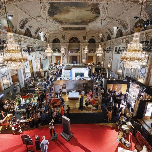 Eine Veranstaltung findet in einem opulenten Saal mit Kronleuchtern und vielen Menschen statt.
