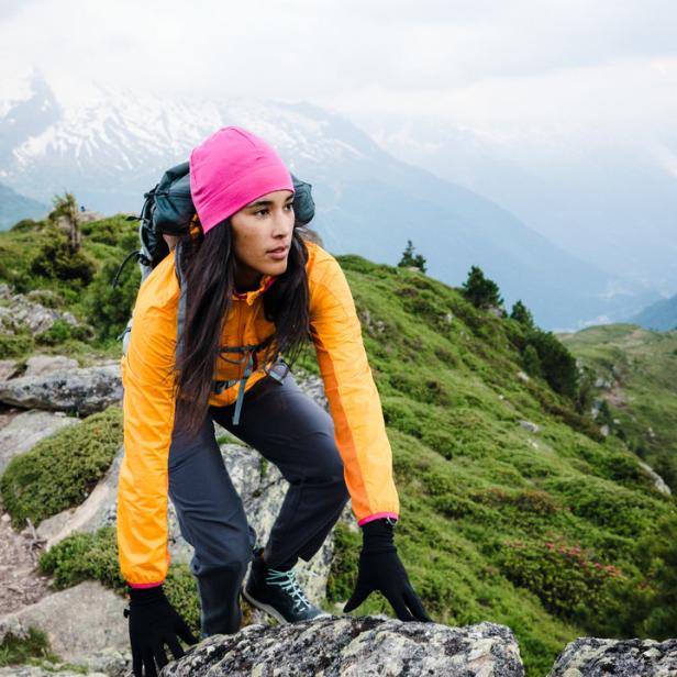 Eine Frau klettert mit Rucksack auf einen Felsen in den Bergen.