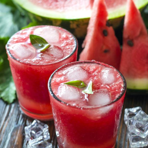 Zwei Gläser Wassermelonensaft mit Eiswürfeln und Melonenscheiben im Hintergrund.